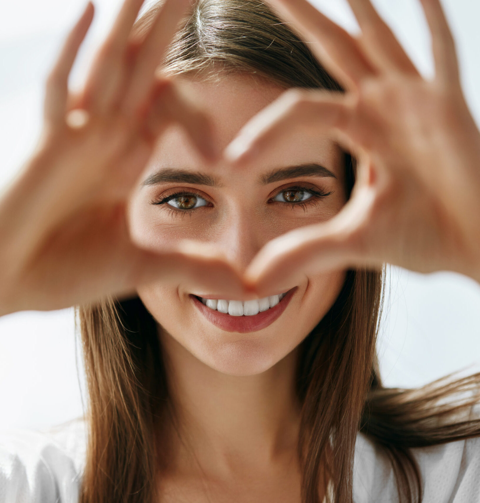 Healthy Eyes And Vision. Portrait Of Beautiful Happy Woman Holding Heart Shaped Hands Near Eyes. Closeup Of Smiling Girl With Healthy Skin Showing Love Sign. Eyecare. High Resolution Image