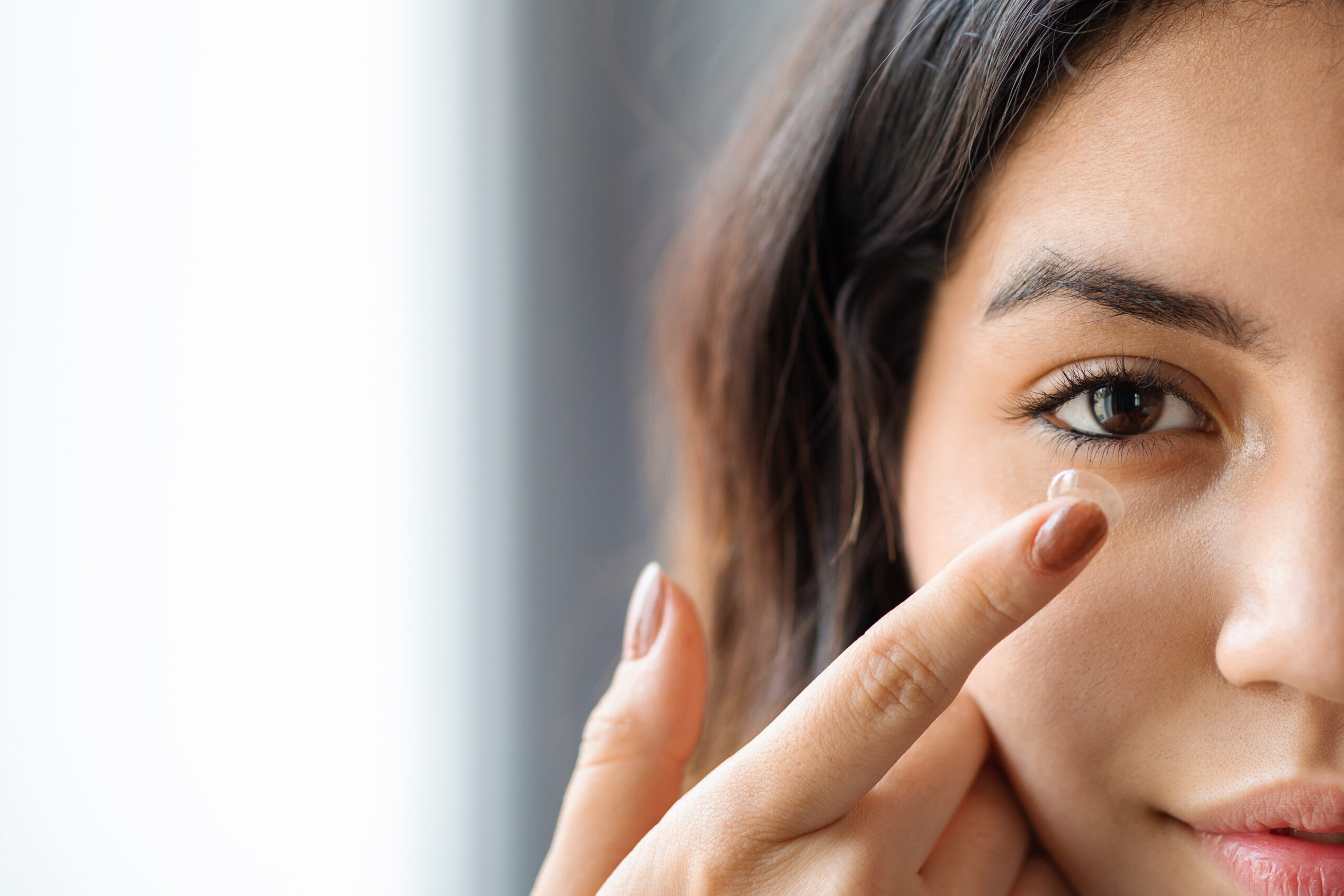 Ophthalmology Care Concept. Young arab woman putting contact lens in her eye at home, closeup macro shot of middle eastern female with brown eyes applying or removing soft contacts, cropped